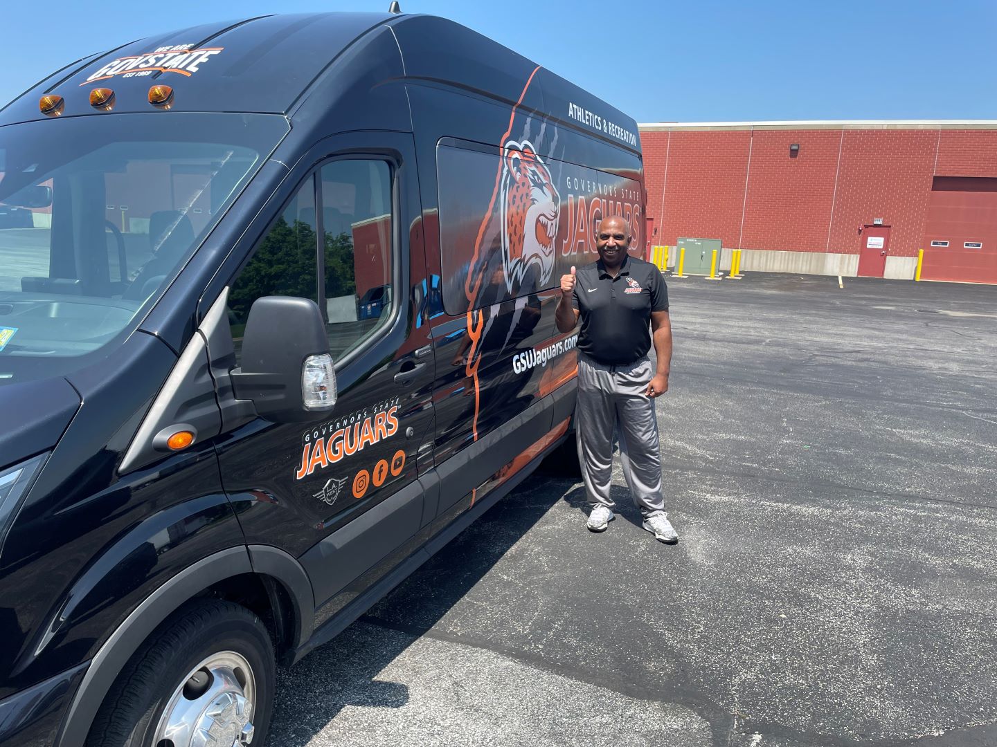 Governors State University Athletic Director and Head Men's Basketball Coach Tony Bates pictured with one of the two Jaguars teams vans all outfitted and new painting for the 2024-2025 athletic seasons.